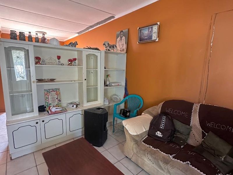 A living room featuring tiled flooring, a built-in display cabinet, and coved ceiling details, offering a functional space with potential for cosmetic updates.