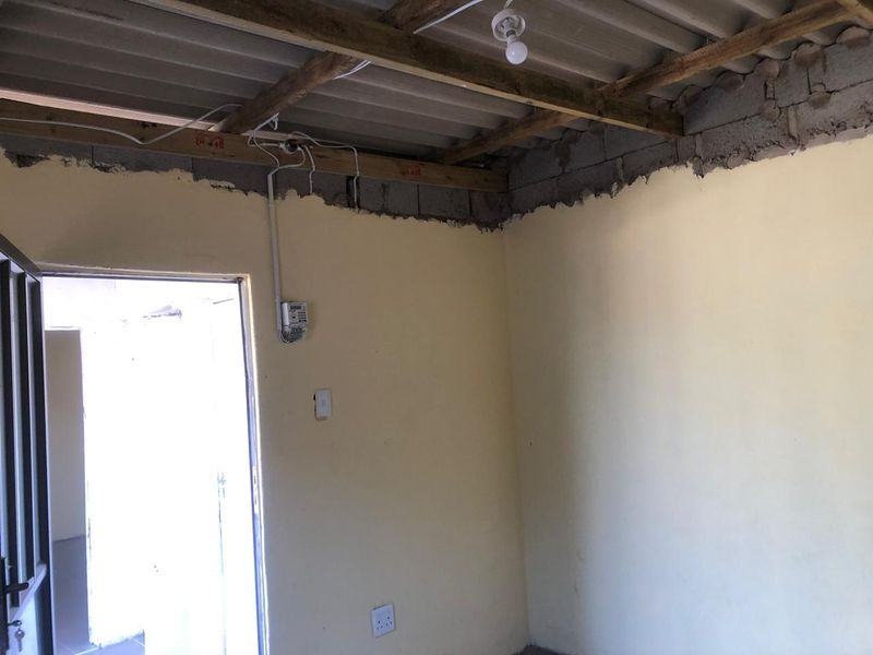 An unfinished interior room featuring exposed timber roof trusses, corrugated roofing, and exposed masonry, presenting a blank canvas for renovation.