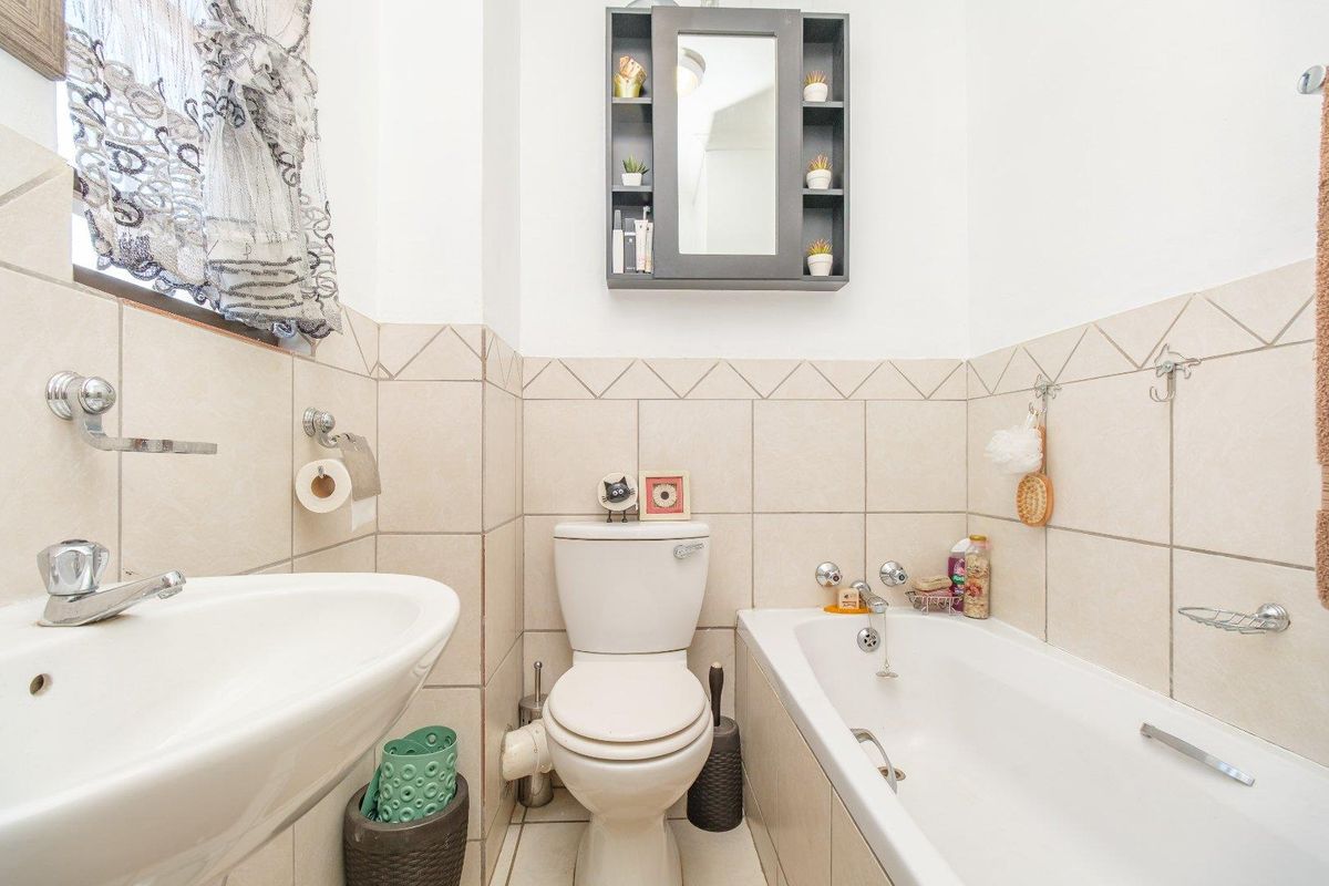 A functional bathroom featuring a pedestal basin, toilet, and bathtub with neutral wall tiling and a wall-mounted mirror cabinet.