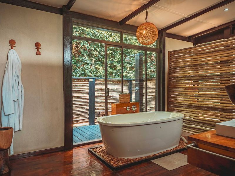 Luxurious bathroom featuring a freestanding bathtub, vessel sink, and seamless transition to a private outdoor shower area with timber privacy screening.