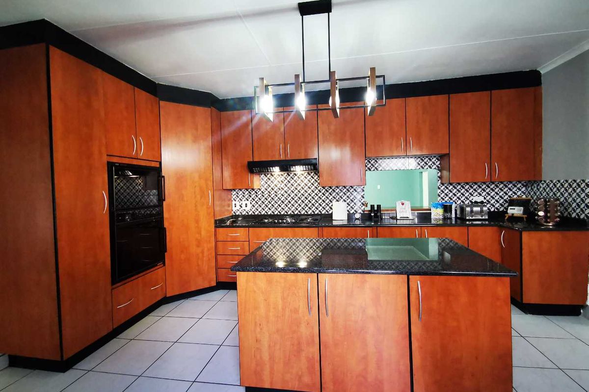 Spacious kitchen featuring warm-toned wooden cabinetry, granite countertops, a central island, built-in oven, and a gas hob with a decorative tiled backsplash.