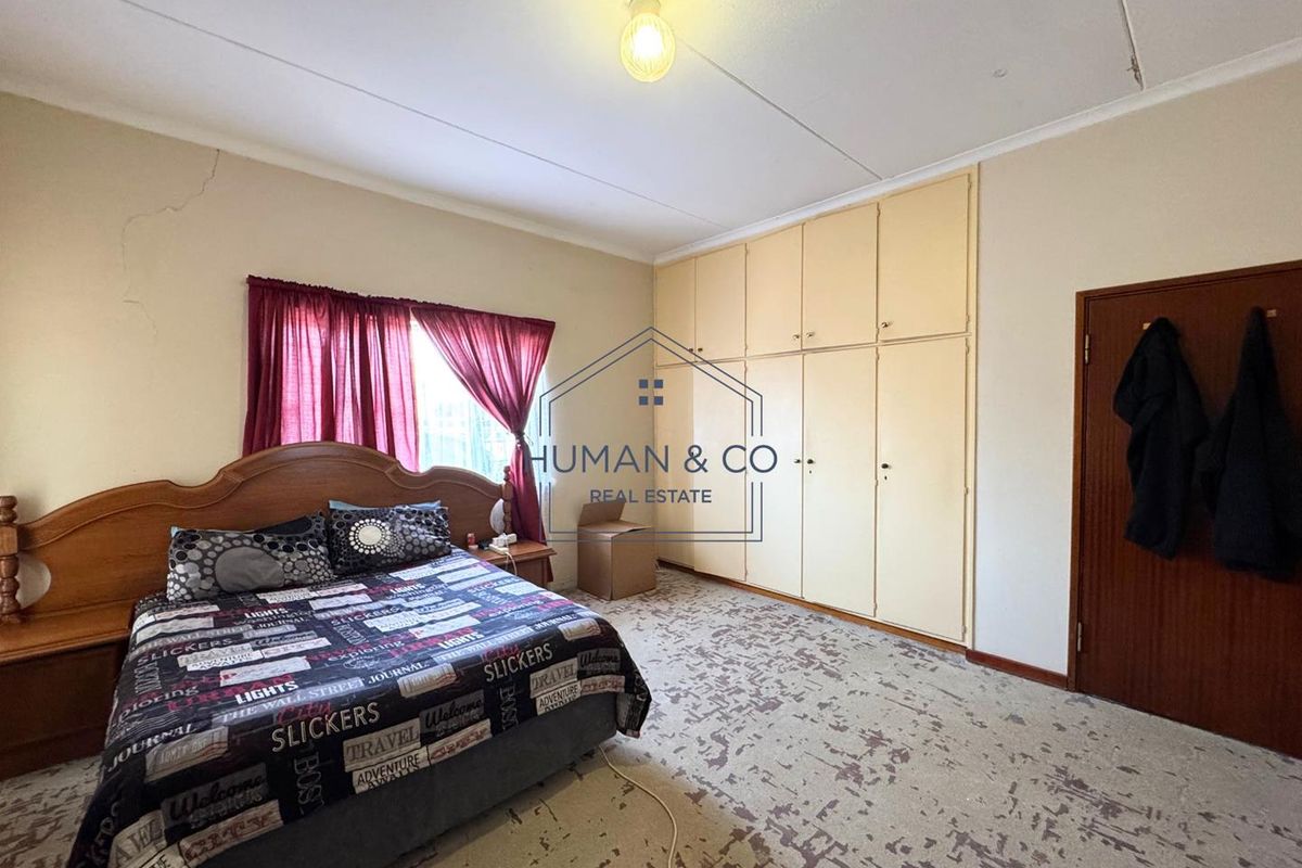 A bedroom featuring built-in cupboards, carpeted flooring, and a window with curtains. The room shows signs of wear and requires cosmetic updates.