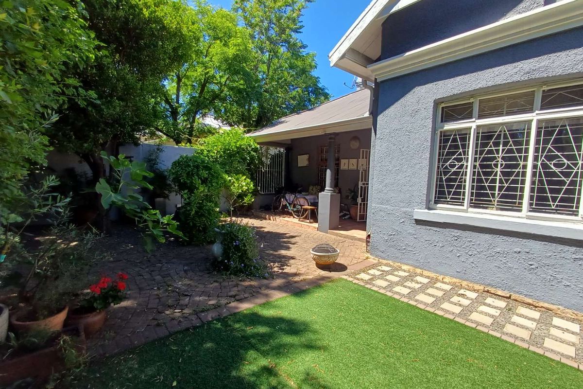 A view of the rear garden featuring a paved patio area, a small lawn, and established trees adjacent to the house exterior.