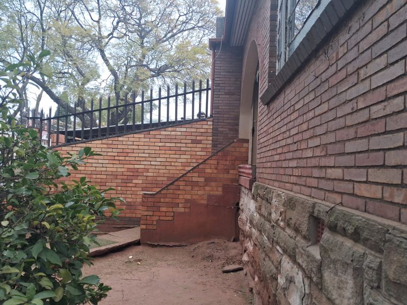 Exterior view of the property showing brick and stone wall construction, metal security fencing, and concrete steps leading to the side entrance.