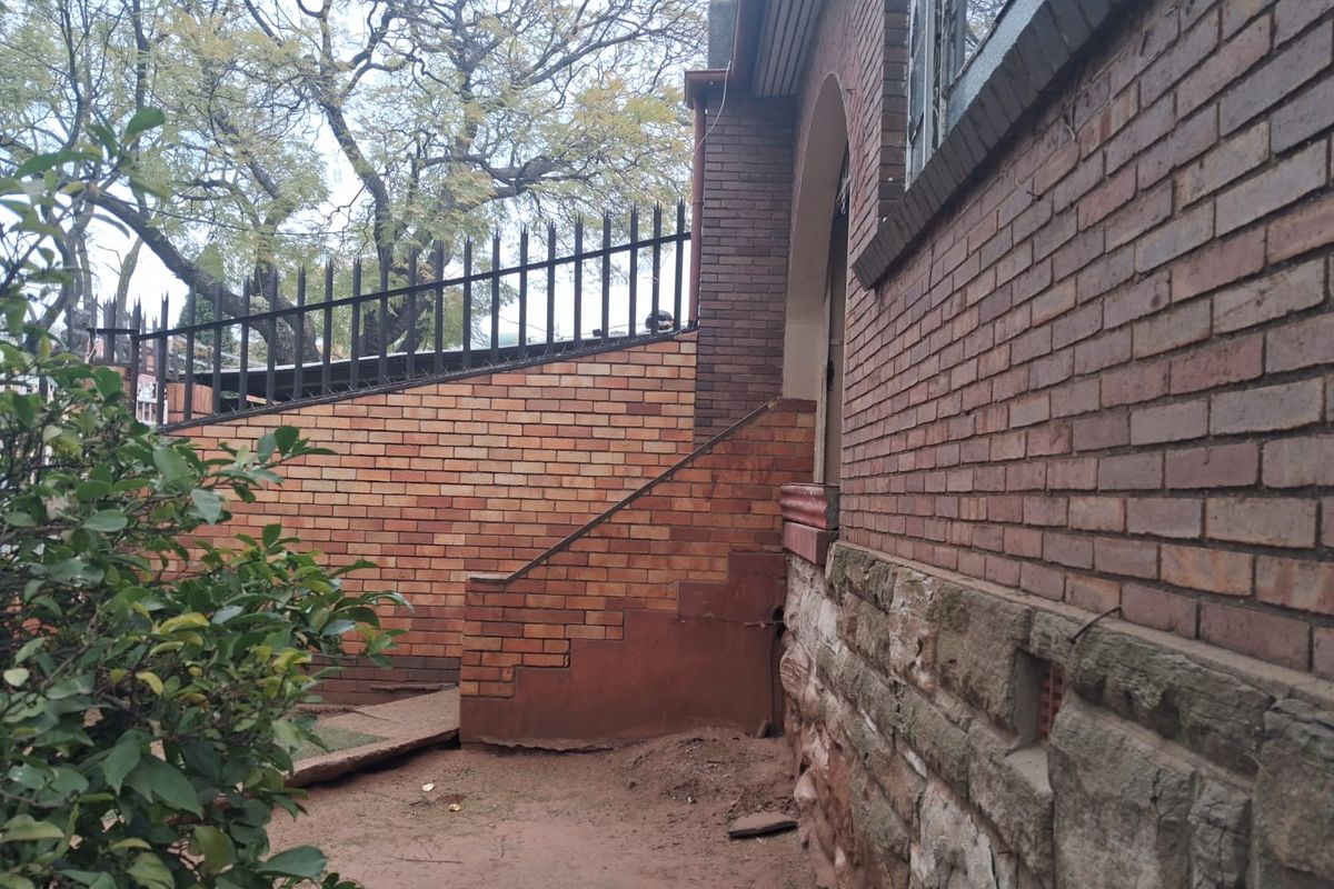 Exterior view of the property showing brick and stone wall construction, metal security fencing, and concrete steps leading to the side entrance.