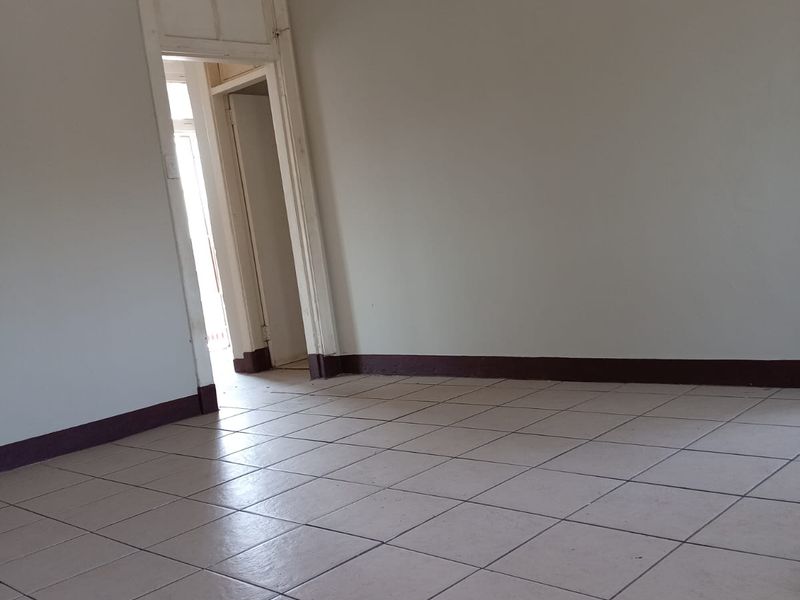 An empty living room featuring tiled flooring, decorative ceiling cornicing, and a classic ceiling rose, providing a blank canvas for interior design.