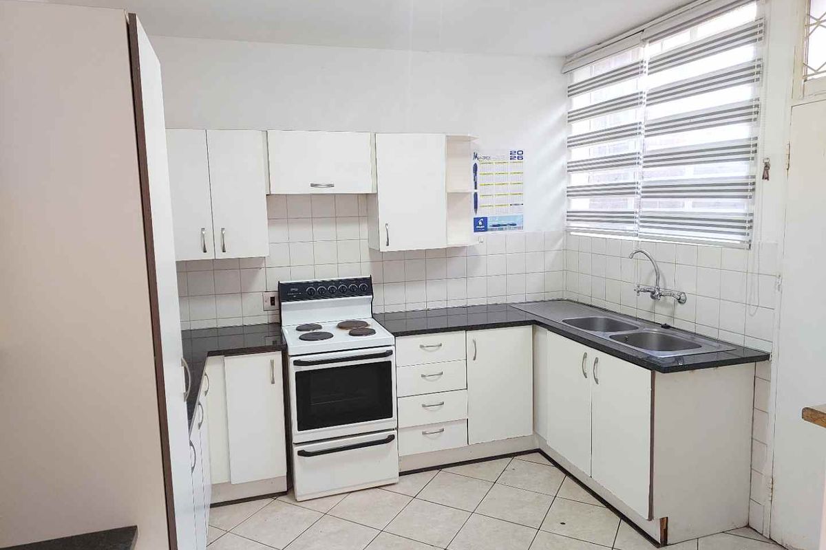 Functional kitchen featuring white cabinetry, dark countertops, a double bowl sink, and a freestanding stove with tiled flooring and backsplash.