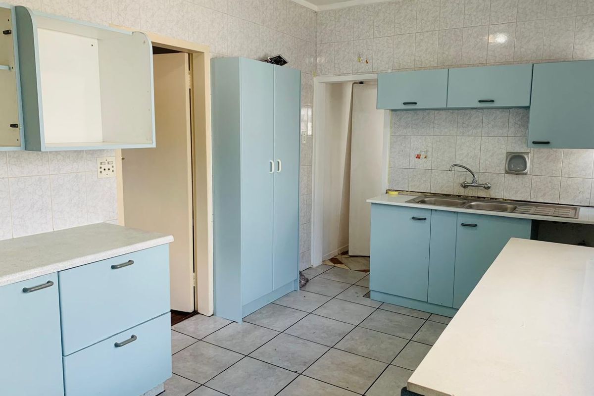 A dated kitchen featuring light blue built-in cabinetry, tiled walls, and tiled flooring, offering a blank canvas for a modern renovation.