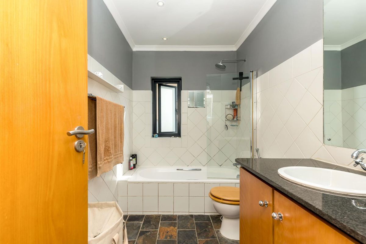 A functional bathroom featuring a built-in vanity with granite countertop, a bathtub with glass shower screen, and tiled finishes throughout.