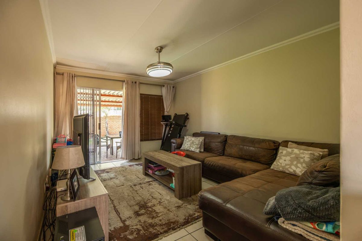 A comfortable living room featuring tiled flooring, a ceiling fan, and a sliding glass door providing access to the outdoor patio area.