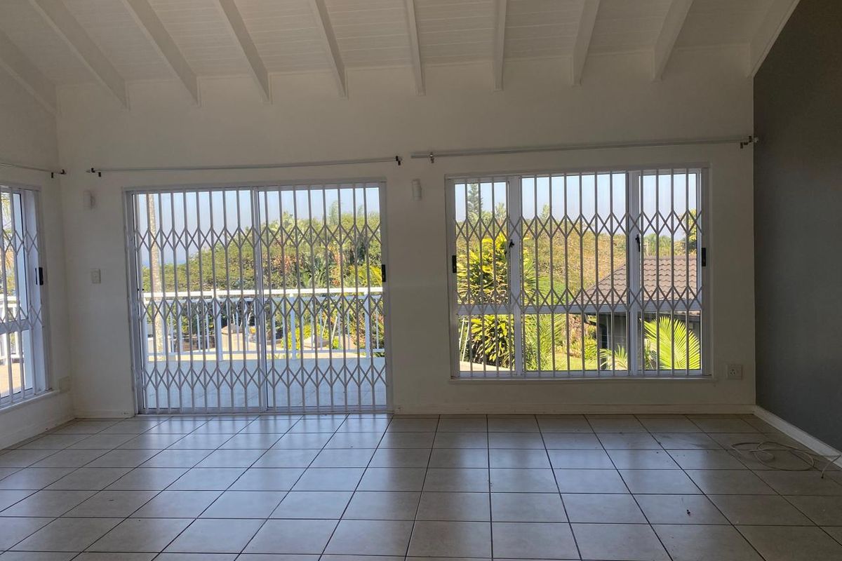 Spacious living area featuring vaulted ceilings, tiled flooring, and large windows with security gates, offering natural light and views of the garden.