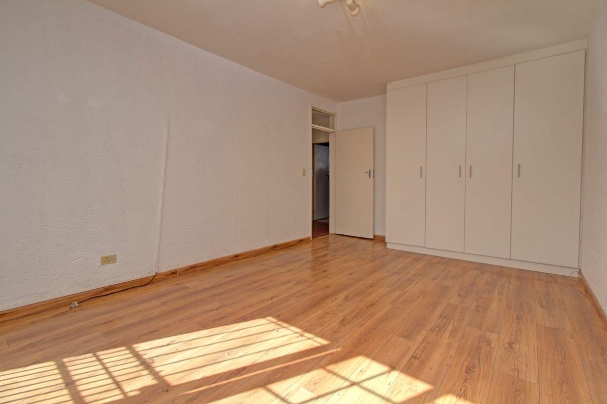 A bright, empty bedroom featuring light wood-look laminate flooring and built-in white cabinetry with ample storage space.