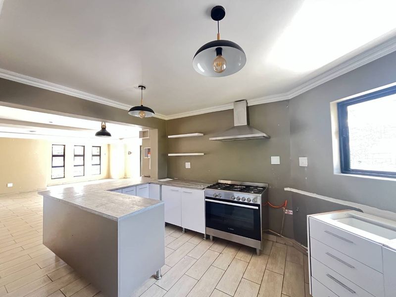 Modern open-plan kitchen featuring stainless steel gas stove, extractor fan, stone-look countertops, and tiled flooring, ready for final finishing touches.