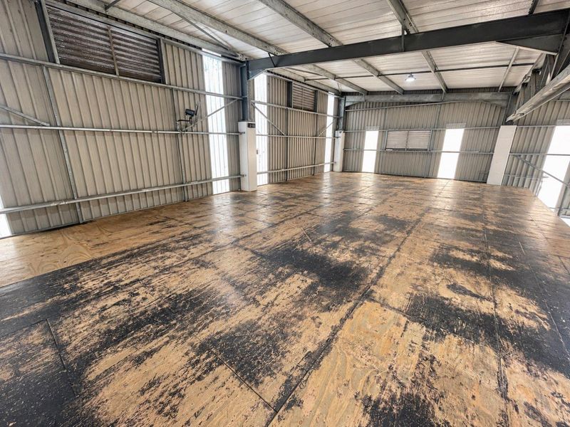 A large, open-plan utility or industrial space featuring exposed steel framing, corrugated metal walls, and worn plywood flooring, suitable for various commercial or storage uses.
