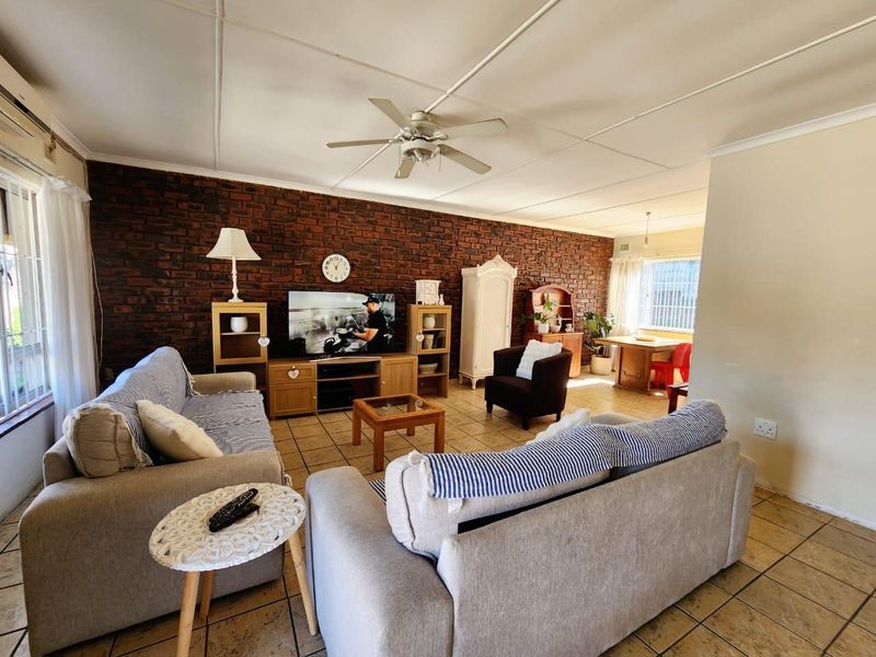 Spacious open-plan living and dining area featuring an exposed brick feature wall, tiled flooring, and a ceiling fan.