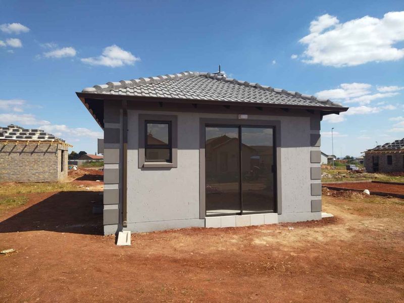 A newly constructed residential unit featuring a tiled roof, plastered exterior walls with corner detailing, and a sliding glass door entrance.