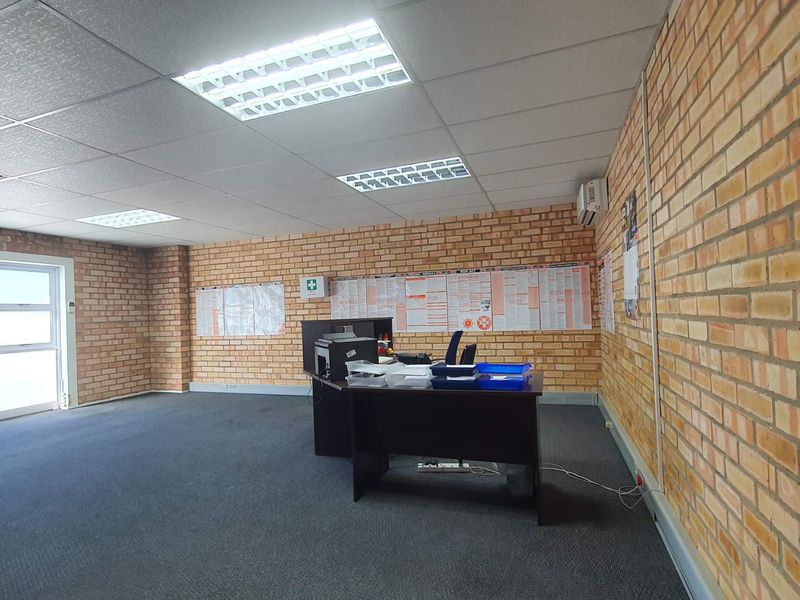 A functional office space featuring exposed brick walls, carpeted flooring, and a suspended ceiling with recessed lighting.