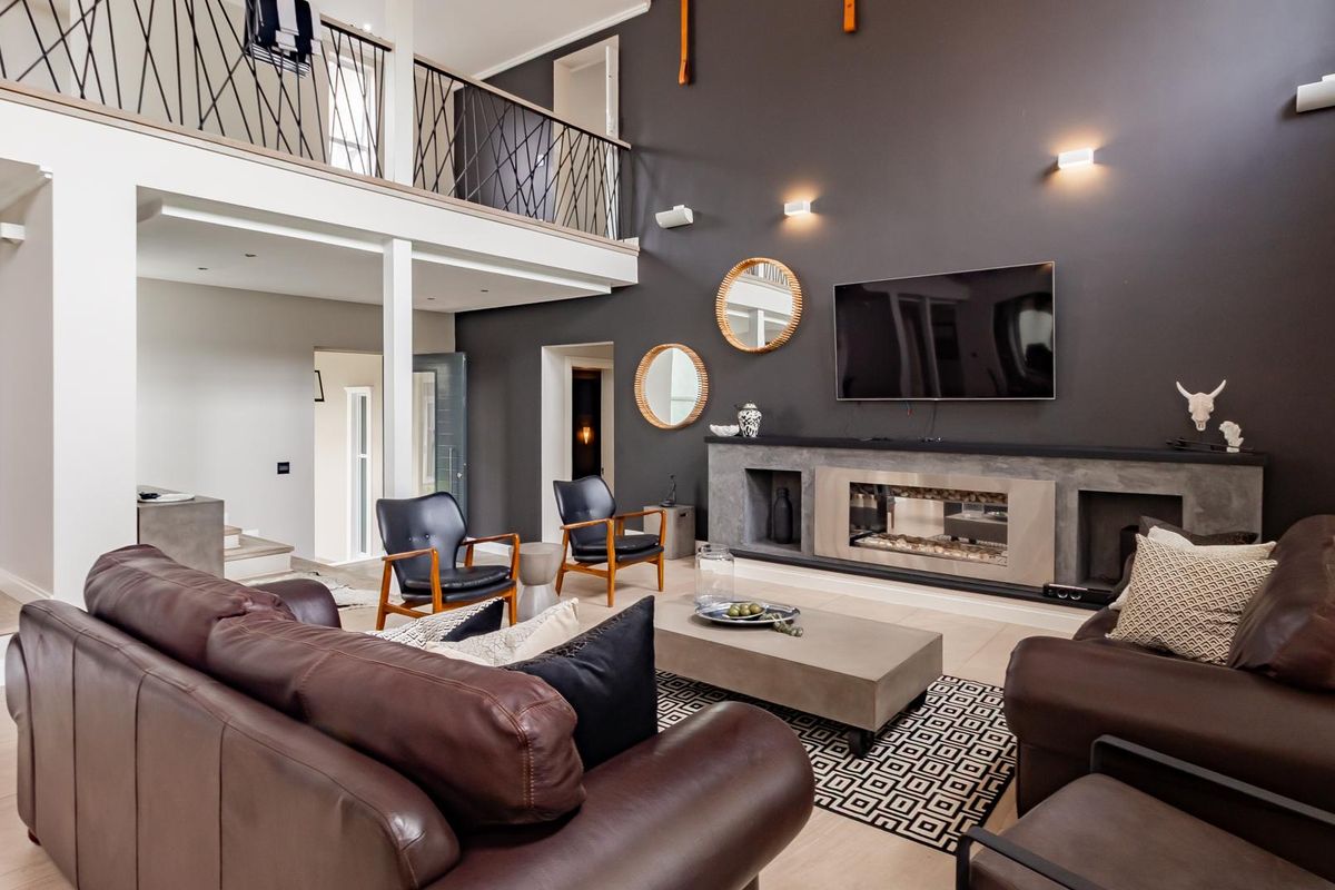 Spacious double-volume living room featuring a modern built-in fireplace, dark feature wall, and an open mezzanine balcony overlooking the main seating area.