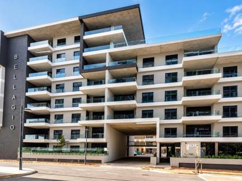 Modern multi-story apartment building facade featuring contemporary concrete architecture, glass balcony railings, and a prominent ground-level entrance.