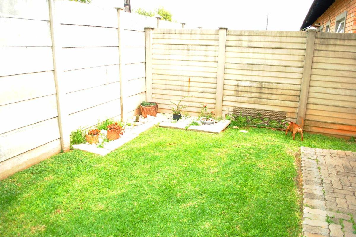 A private rear garden area featuring a small lawn, paved border, and enclosed by precast concrete boundary walls.