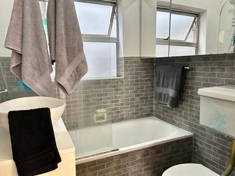 A functional bathroom featuring a bathtub with a glass screen, vessel sink vanity, and grey subway-style wall tiling.