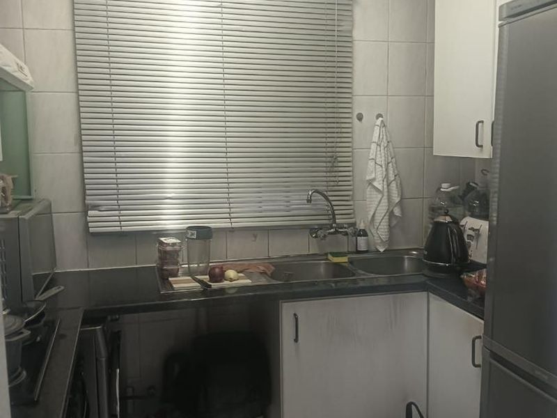 Compact kitchen featuring white cabinetry, dark countertops, tiled backsplash, and a double sink with a window view.
