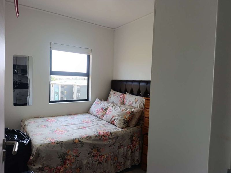 A compact bedroom featuring a window with a roller blind, providing natural light and a view of the surrounding apartment complex.