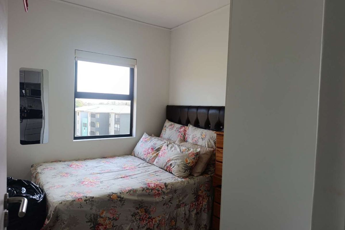 A compact bedroom featuring a window with a roller blind, providing natural light and a view of the surrounding apartment complex.