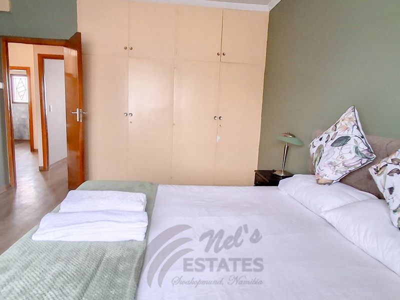 A bedroom featuring built-in cupboards, laminate flooring, and direct access to the hallway.