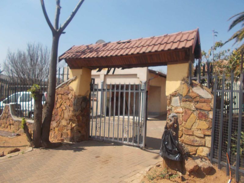 Front entrance featuring a stone-clad gate structure with a tiled roof and metal security gate leading to the property driveway.
