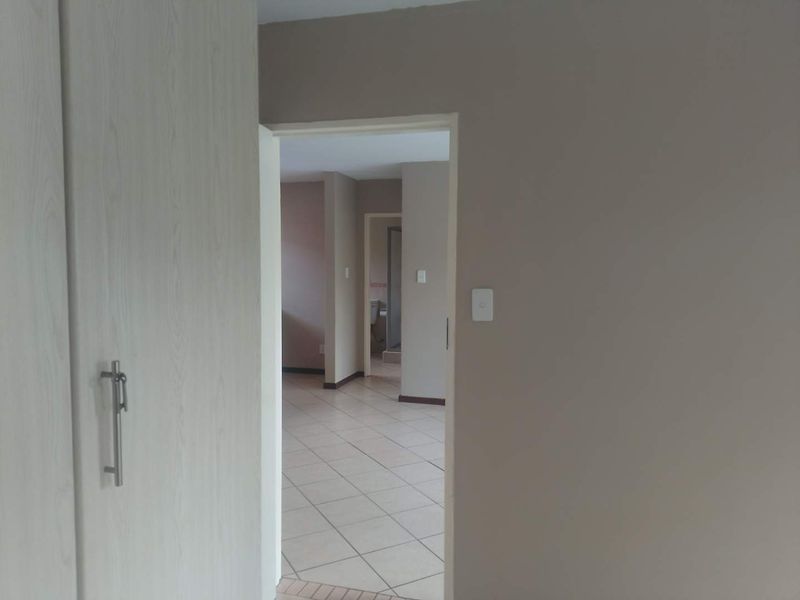 A view through a hallway featuring neutral wall tones, tiled flooring, and built-in cupboard storage, leading into adjacent living spaces.