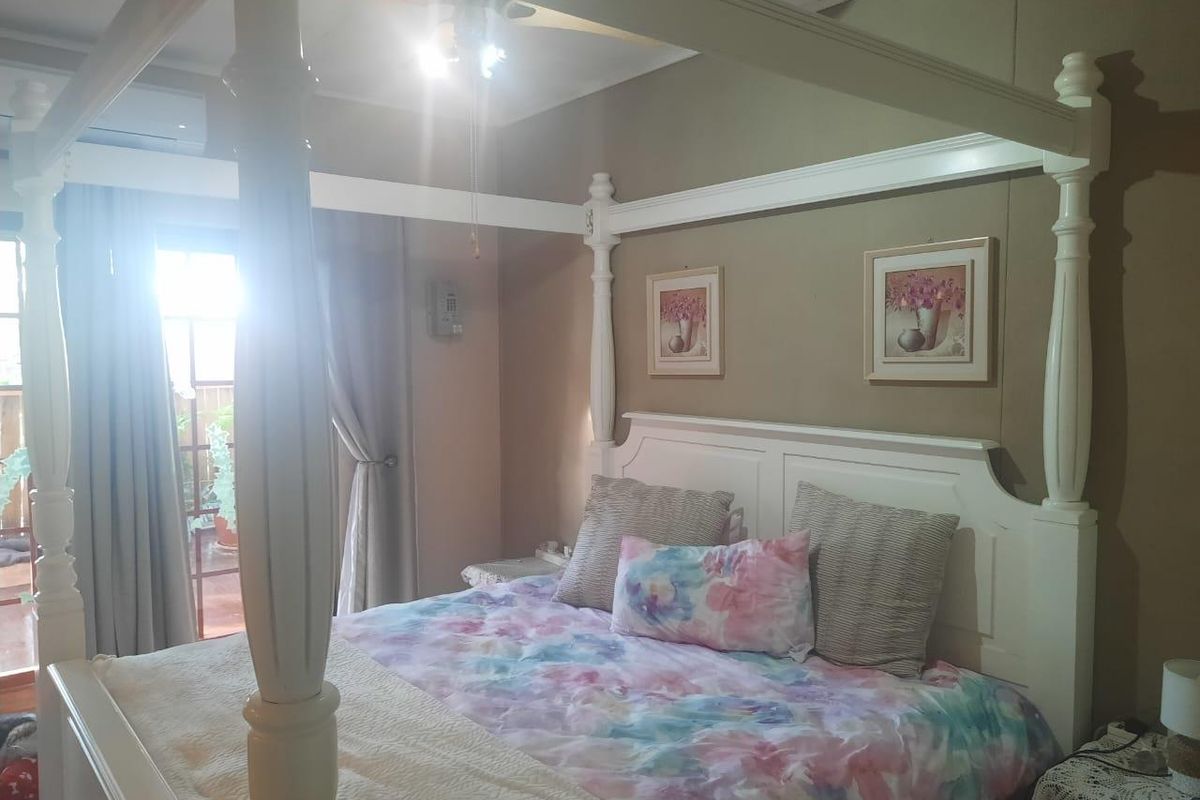 A bedroom featuring a four-poster bed frame, neutral wall tones, and direct access to an outdoor area through a glass sliding door.