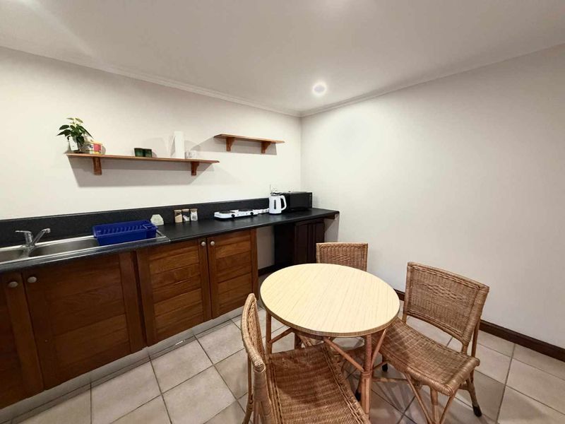 A compact kitchen area featuring wooden cabinetry, dark laminate countertops, a stainless steel sink, and tiled flooring, providing a functional prep space.