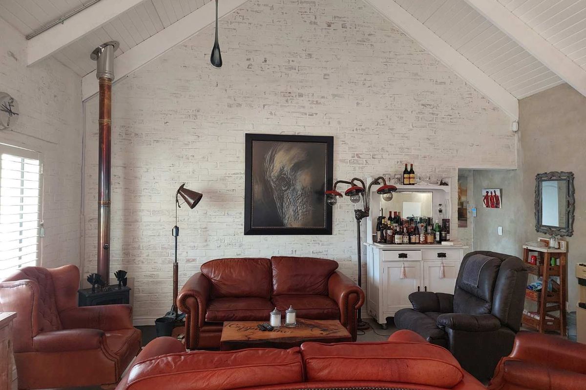 Spacious living room featuring a high vaulted ceiling with exposed timber beams and a striking white-painted brick feature wall with a wood-burning stove.
