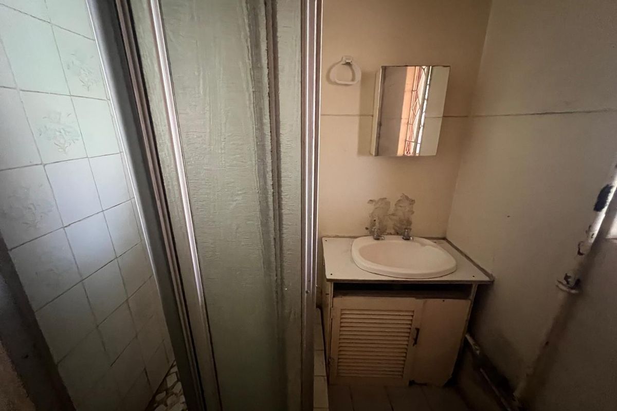 A dated bathroom featuring a shower enclosure, a vanity unit with a wash basin, and a wall-mounted mirror cabinet, requiring cosmetic updates.