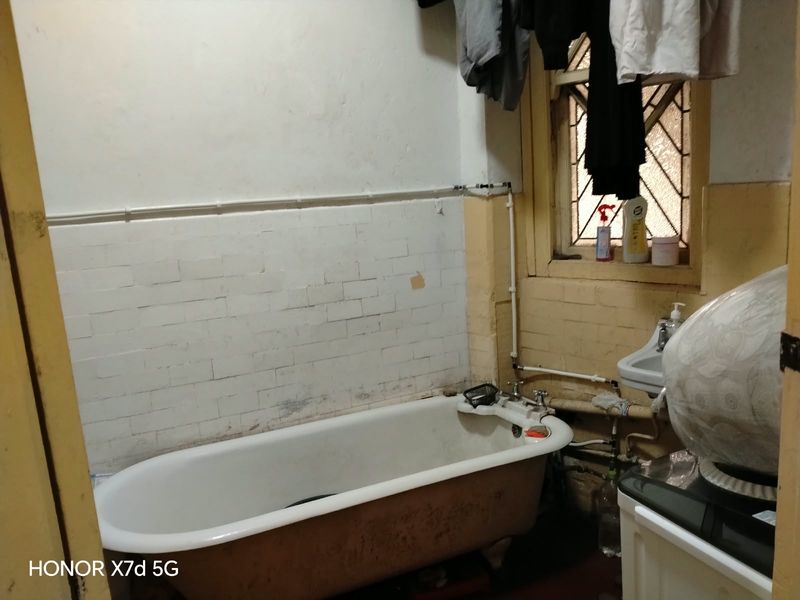 A dated bathroom featuring a vintage bathtub, wall-mounted basin, and exposed plumbing, requiring significant renovation and cosmetic updates to improve functionality and aesthetics.