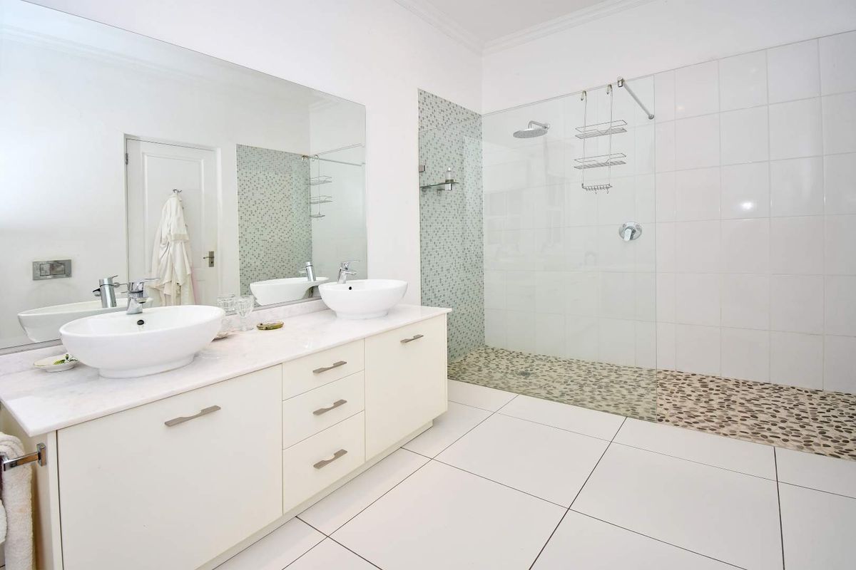 Modern bathroom featuring a double vanity with vessel sinks, a large frameless glass walk-in shower with pebble flooring, and neutral tiled finishes.