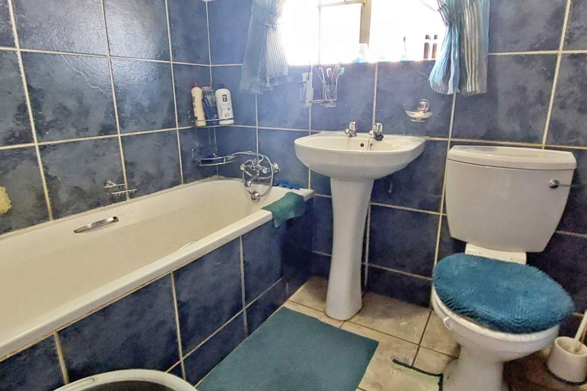 A functional bathroom featuring a standard bathtub, pedestal basin, and toilet, finished with full-height blue wall tiling.