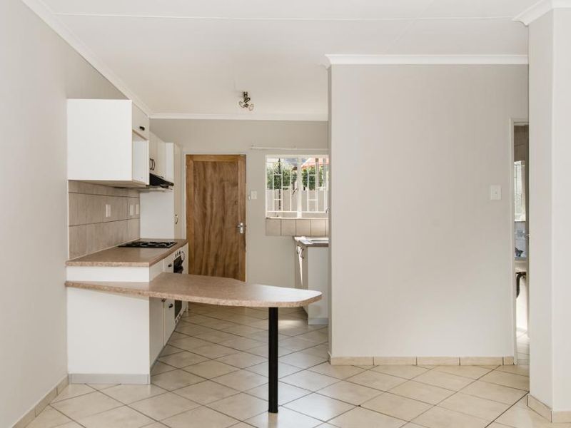 A clean, empty kitchen featuring built-in cabinetry, laminate countertops, an electric hob, and tiled flooring, offering a functional layout ready for personalization.
