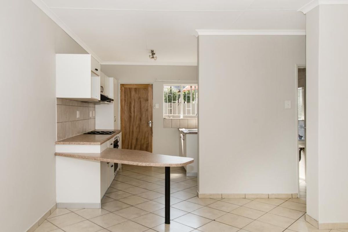 A clean, empty kitchen featuring built-in cabinetry, laminate countertops, an electric hob, and tiled flooring, offering a functional layout ready for personalization.