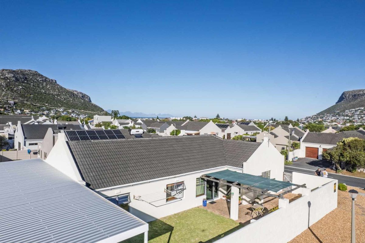 Aerial view of the property showing the rear garden, patio area with pergola, tiled roof, and integrated solar panels against a mountain backdrop.