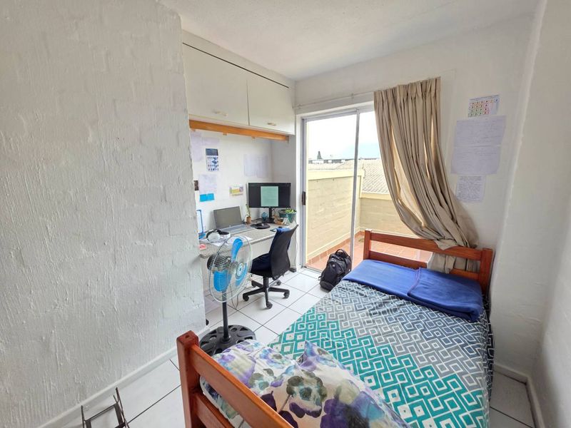 A functional bedroom featuring a built-in desk with overhead storage, tiled flooring, and direct access to a private balcony through sliding glass doors.