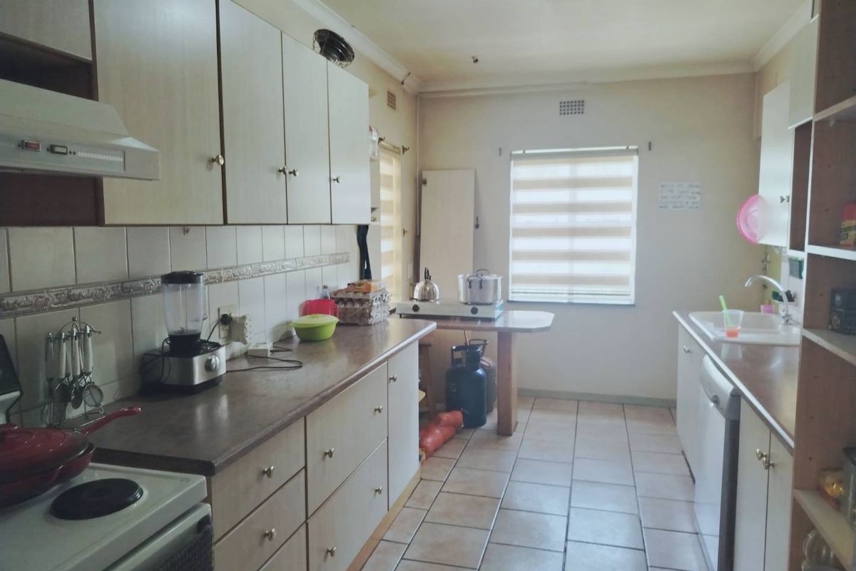 A functional kitchen featuring built-in cabinetry, laminate countertops, tiled flooring, and a double sink, offering a practical layout with potential for modern updates.
