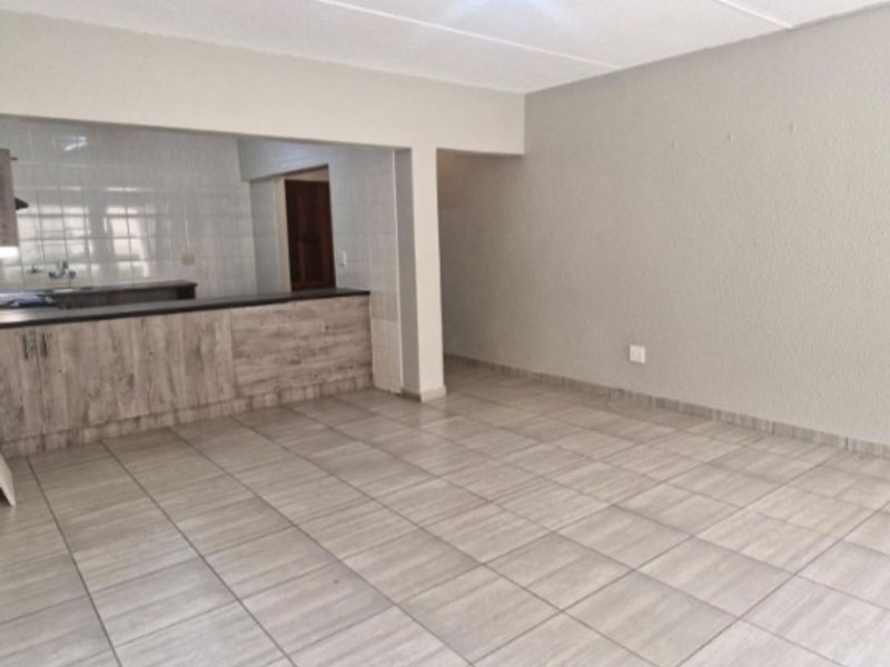 An open-plan living area featuring neutral tiled flooring and a breakfast bar connecting to the kitchen space.