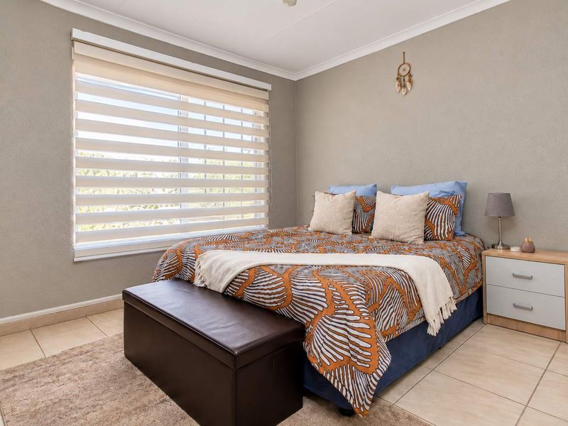 A well-maintained bedroom featuring neutral wall tones, tiled flooring, and modern roller blinds, providing a clean and comfortable living space.