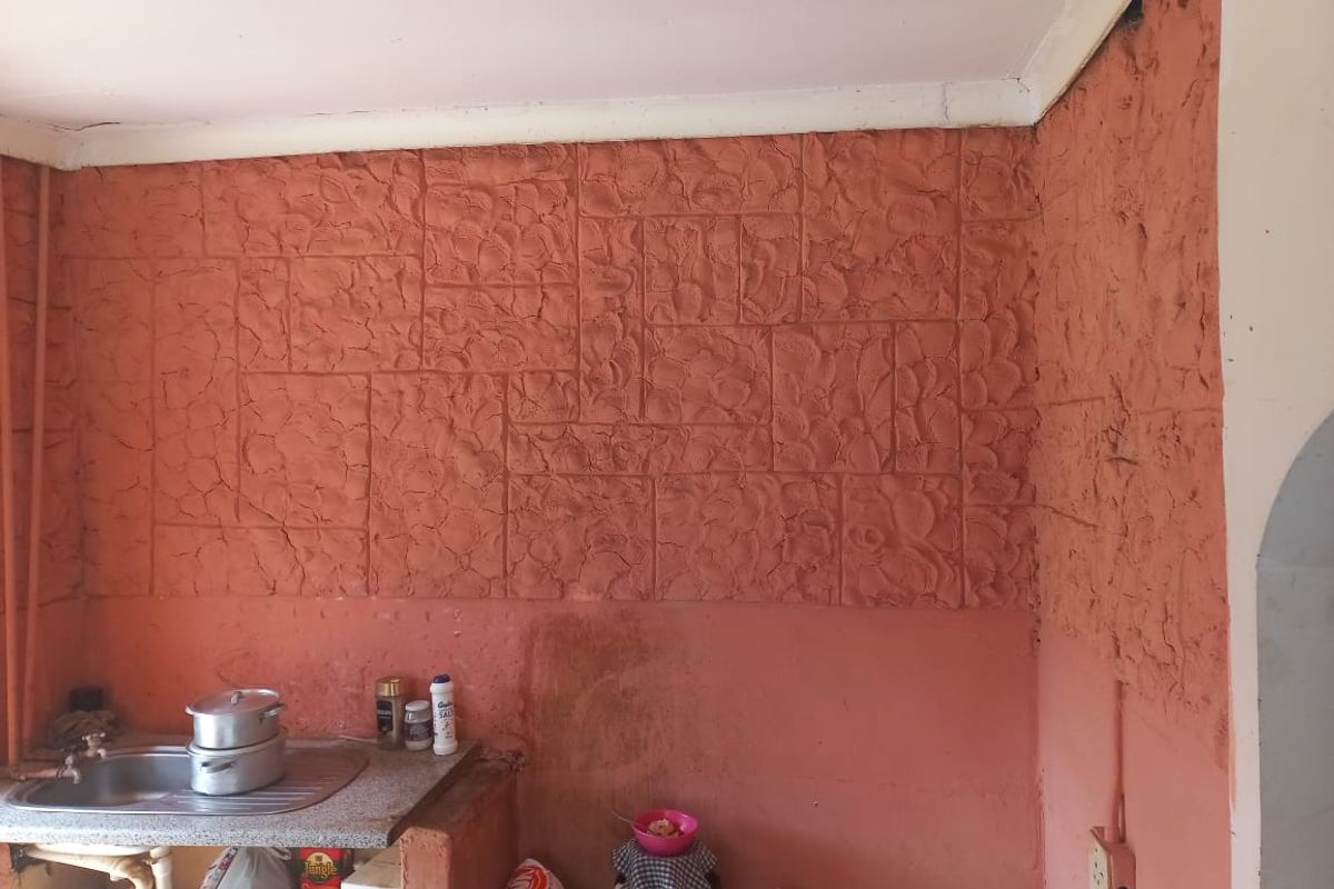 A kitchen area featuring a stainless steel sink and a textured, tiled splashback, requiring cosmetic updates and repairs to the wall finishes.