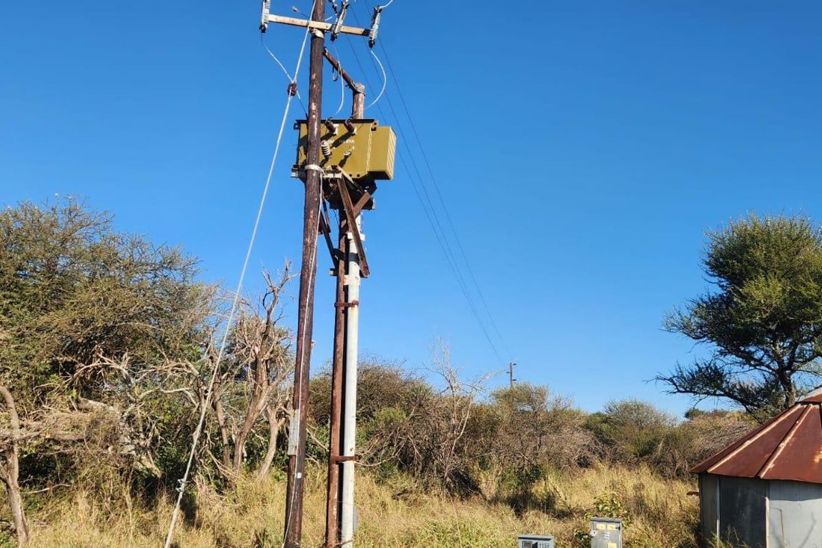 A view of the agricultural land featuring an electrical transformer pole and a small structure with a rusted roof set against natural vegetation.