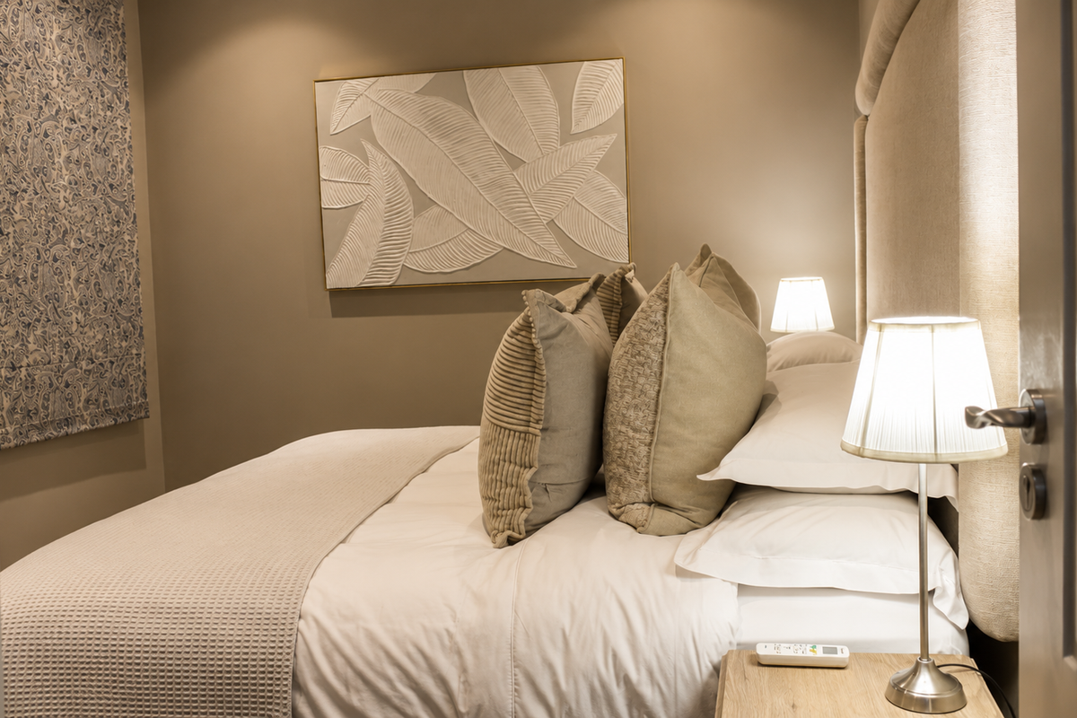 A well-appointed bedroom featuring a neutral color palette, an upholstered headboard, and a patterned roman blind.