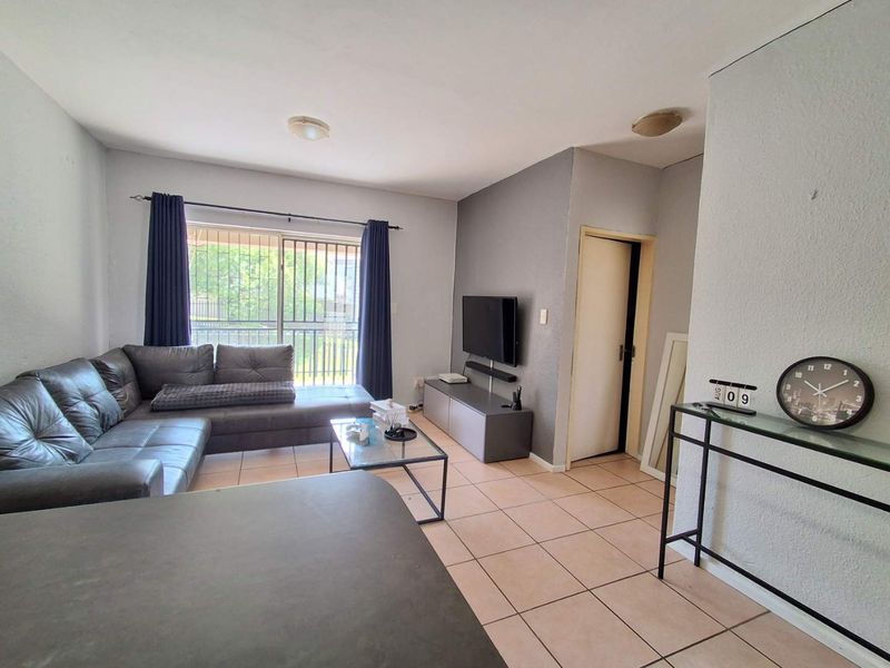 A functional living room featuring tiled flooring, neutral wall tones, and a sliding glass door with security bars providing access to the exterior.