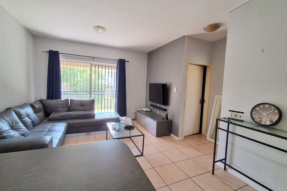 A functional living room featuring tiled flooring, neutral wall tones, and a sliding glass door with security bars providing access to the exterior.
